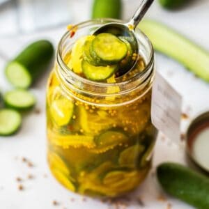 Jar of Bread and Butter Pickles, with a spoon reaching in to lift some pickles out of the jar.