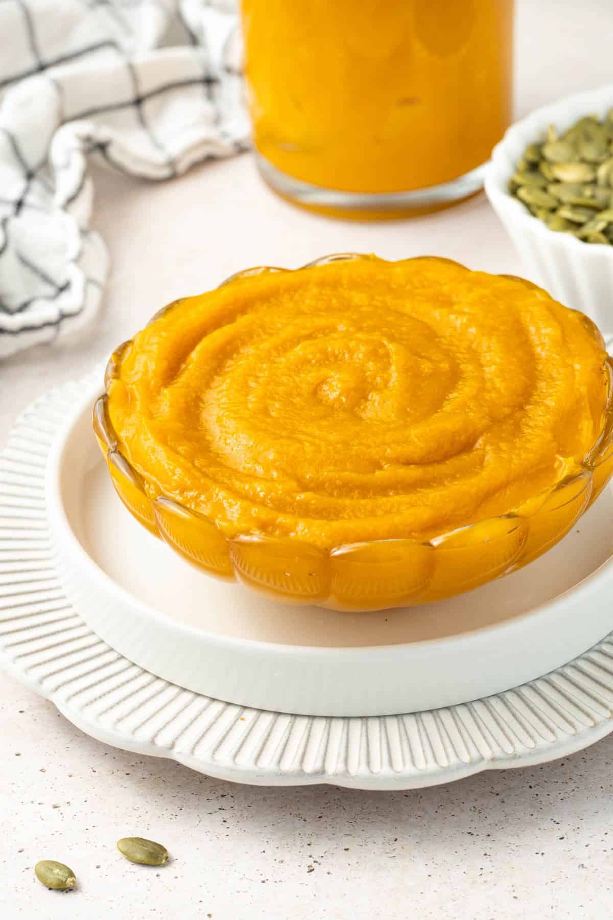 Round glass dish of pumpkin puree, sitting on a white plate.