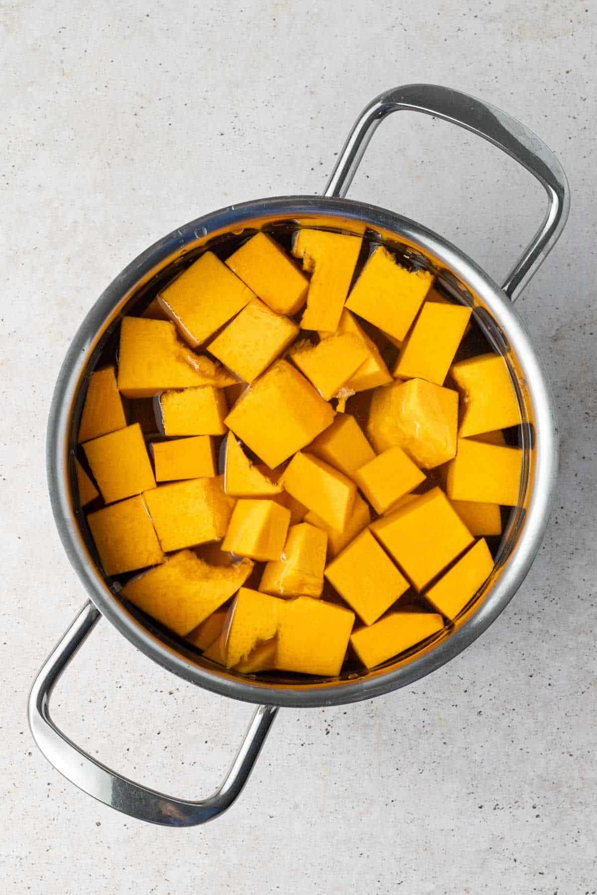 Saucepan full of water with cut pieces of pumpkin ready to be cooked.