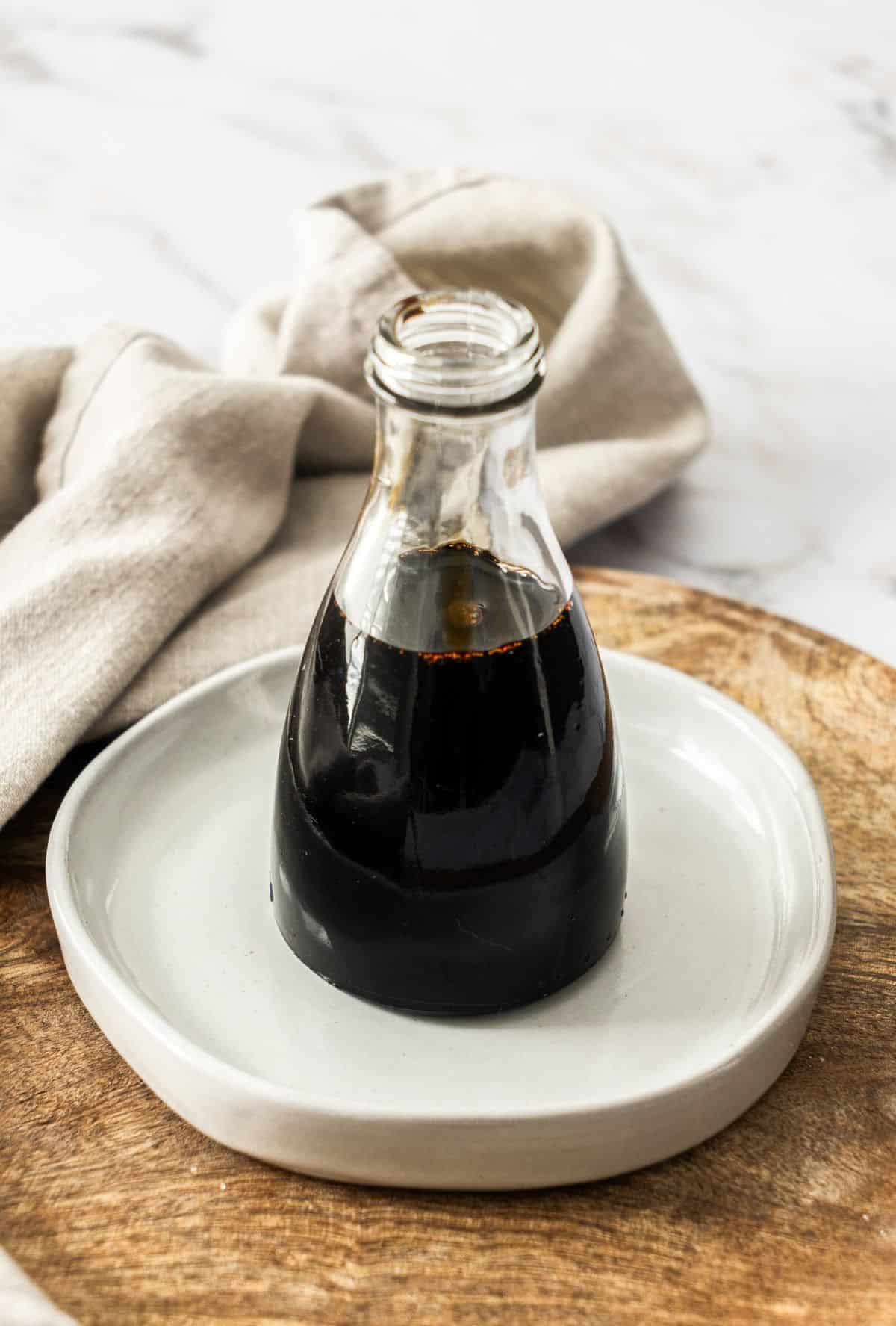 Glass bottle of Balsamic Glaze, sitting on a small round white plate.