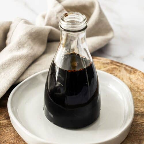 Glass bottle of Balsamic Glaze, sitting on a small round white plate.