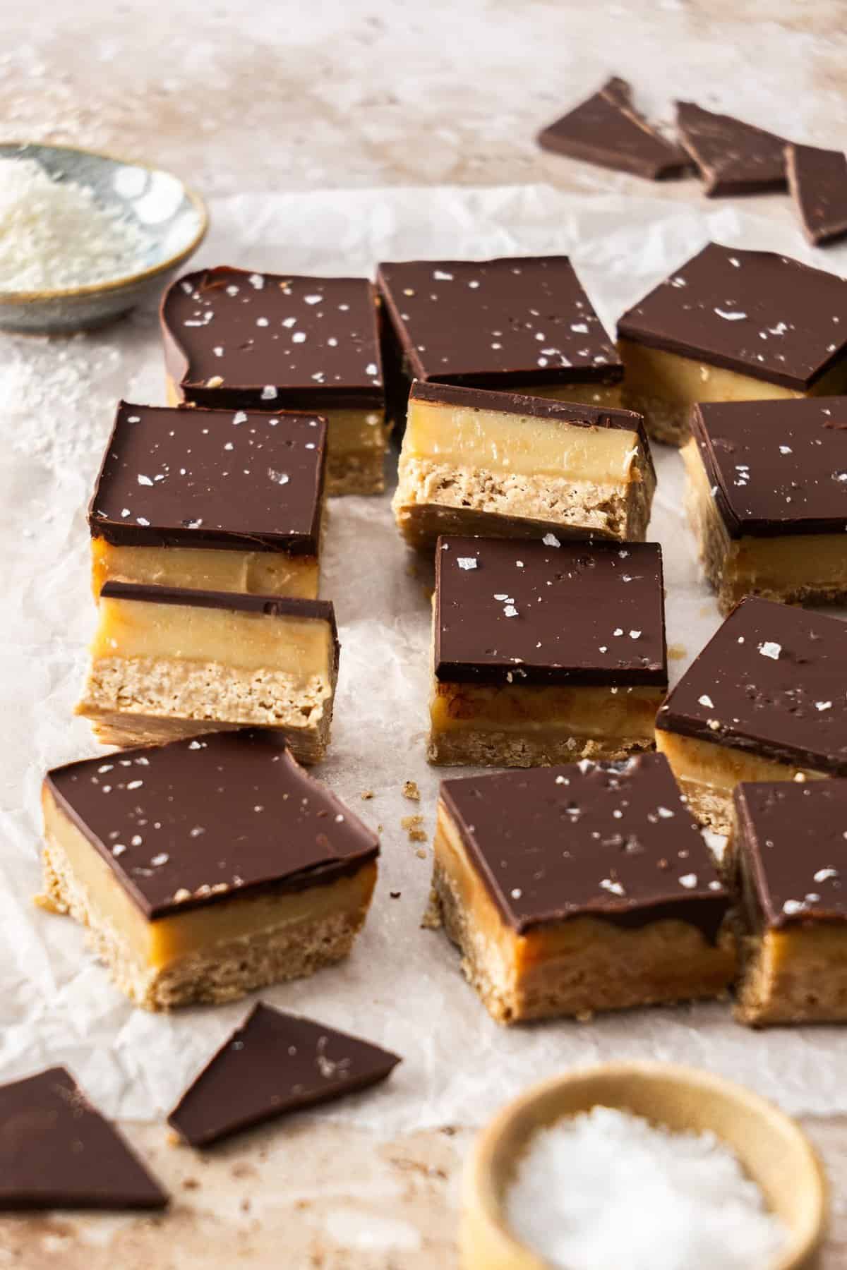 Cut pieces of salted caramel slice, sitting on some baking paper, with a few pieces on the side to show the filling.
