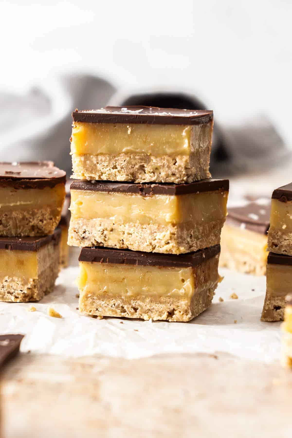 Three pieces of caramel slice stacked on top of each other, with some other pieces on the edge of photo.