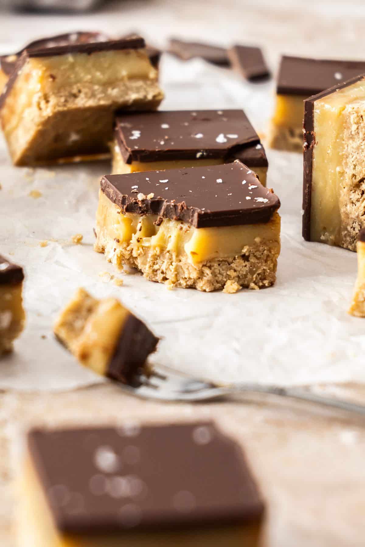 A few pieces of cut caramel slice on baking paper, with one with a small bite taken out of it.