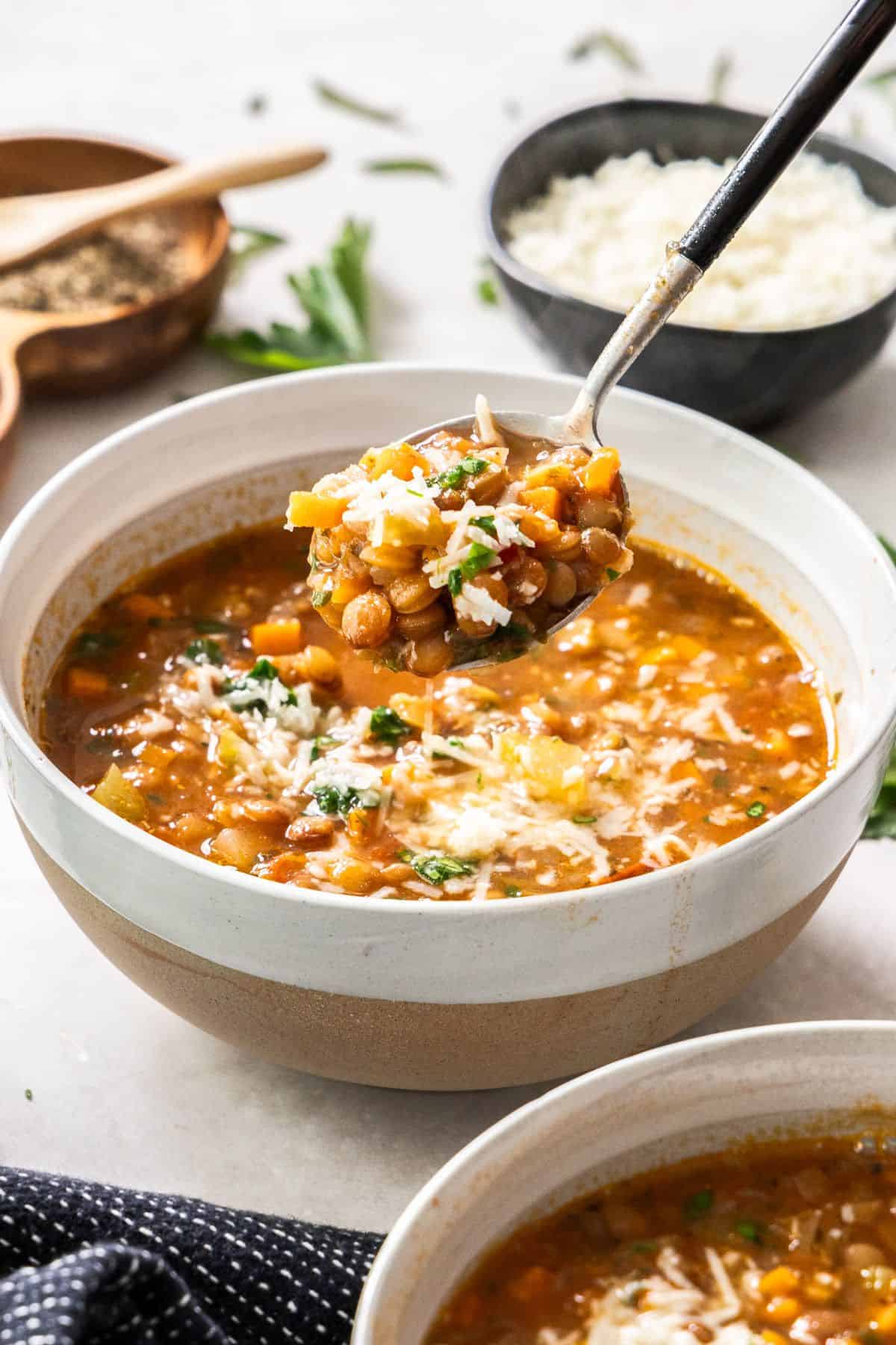 Serve of Lentil Soup in a round white and brown bowl, with a spoon scooping up a mouthful.