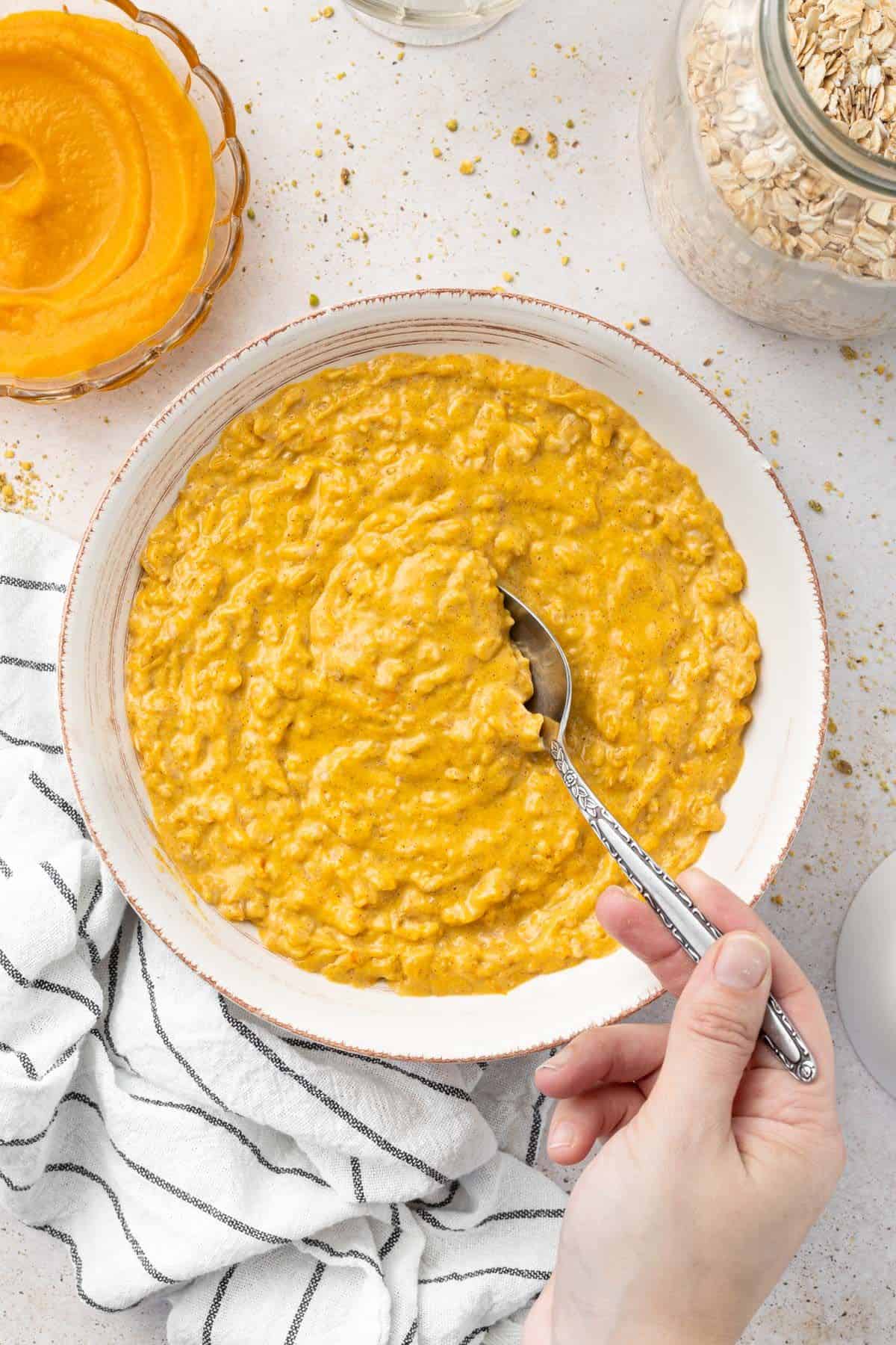 Round white bowl of pumpkin porridge with a spoon scooping up some of the mixture.