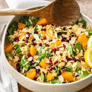 Round cream dish of Quinoa and Spinach Salad, with a wooden serving spoon sitting on the edge.