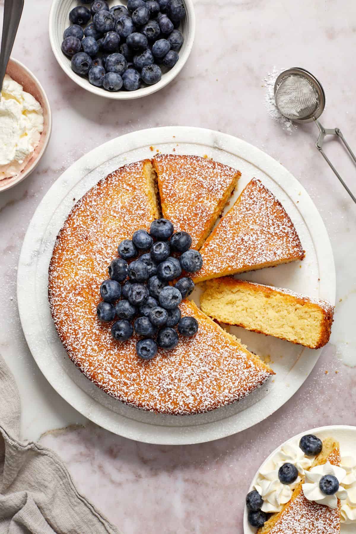 Almond Flour Cake topped with fresh blueberries, with three pieces cut, one lying on side to show texture of cake.