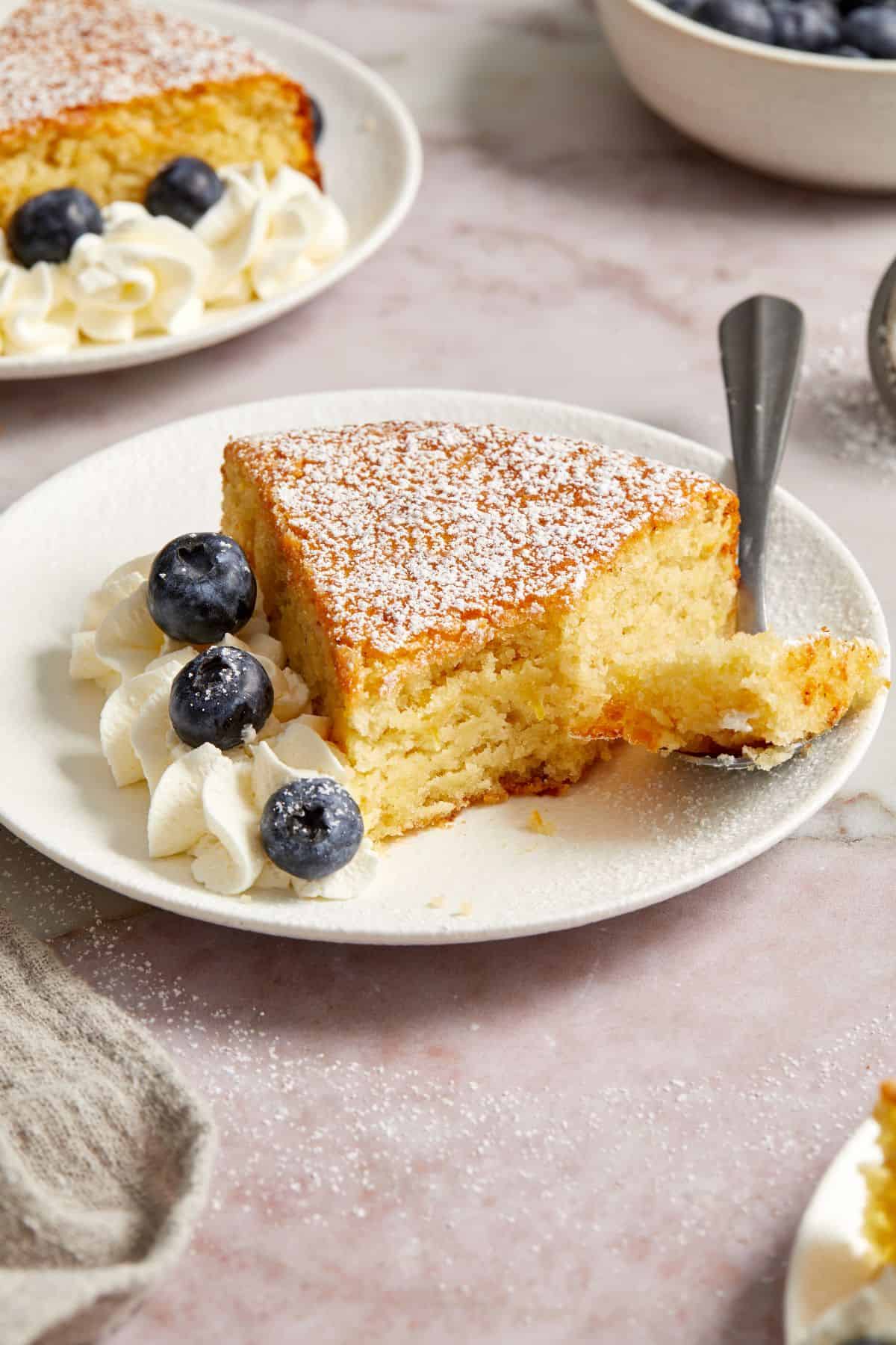 Slice of Almond Flour Cake with a fork cutting into the cake, with some fresh blueberries and whipped cream on the side.