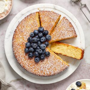 Almond Flour Cake topped with fresh blueberries, with three pieces cut, one lying on side to show texture of cake.