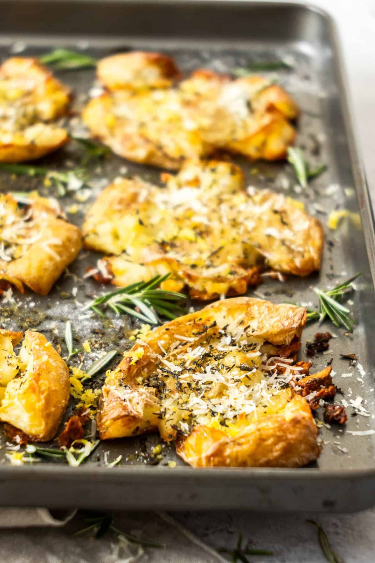 Sheetpan with six roasted Smashed Potatoes, garnished with rosemary, grated Parmesan and lemon zest.