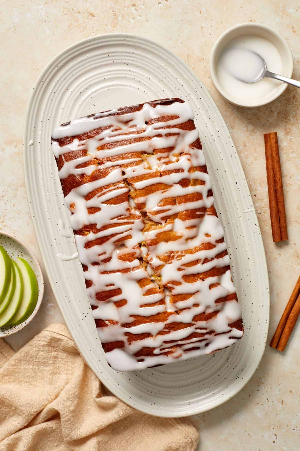 Whole Apple Loaf Cake, sitting on a white oval platter, with a knife on the side.