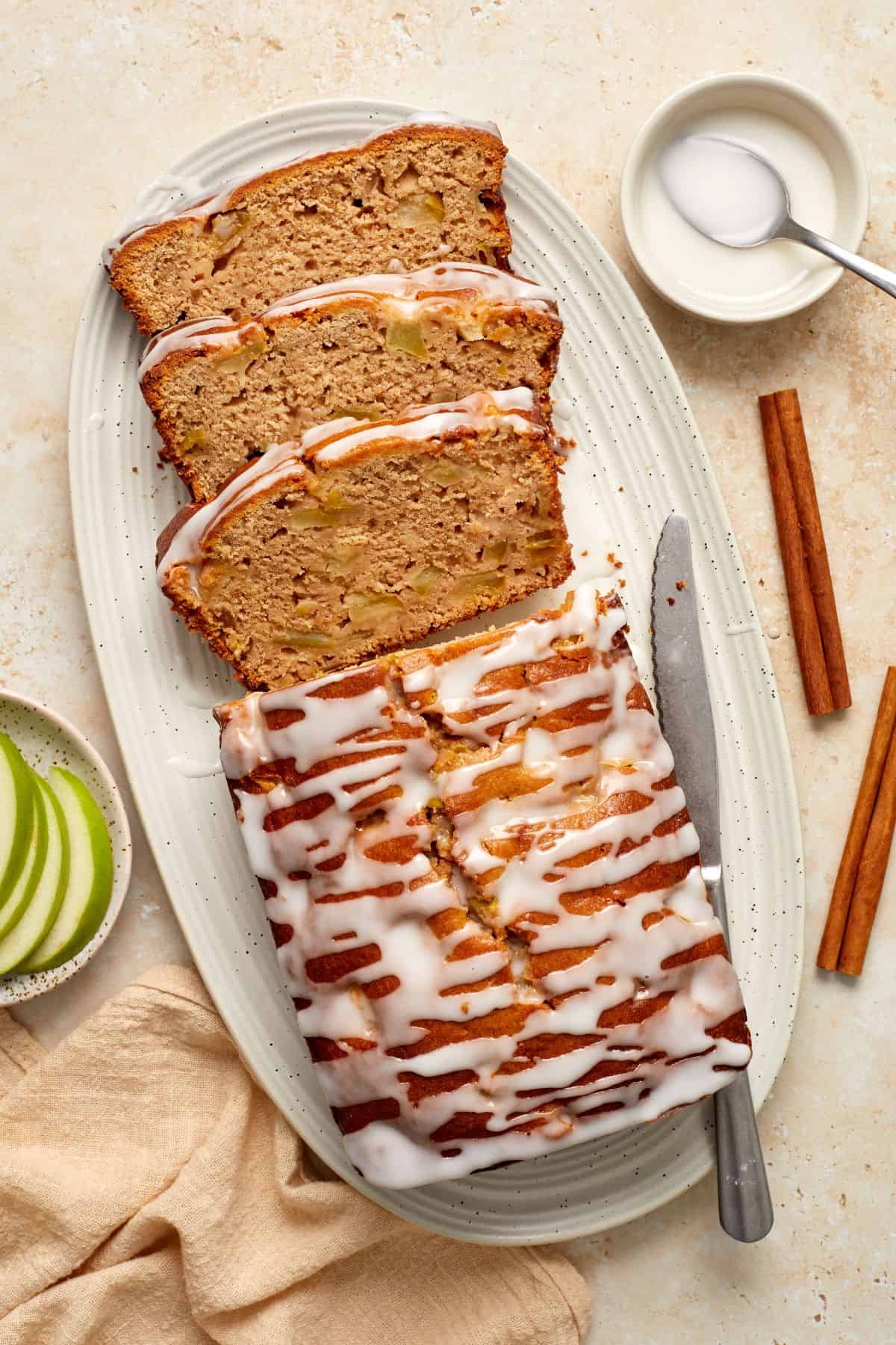 Apple Loaf Cake, with three slices cut, sitting on a white oval platter, with a knife on the side.