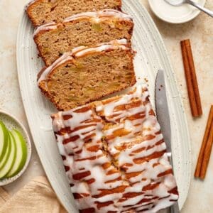 Apple Loaf Cake, with three slices cut, sitting on a white oval platter, with a knife on the side.