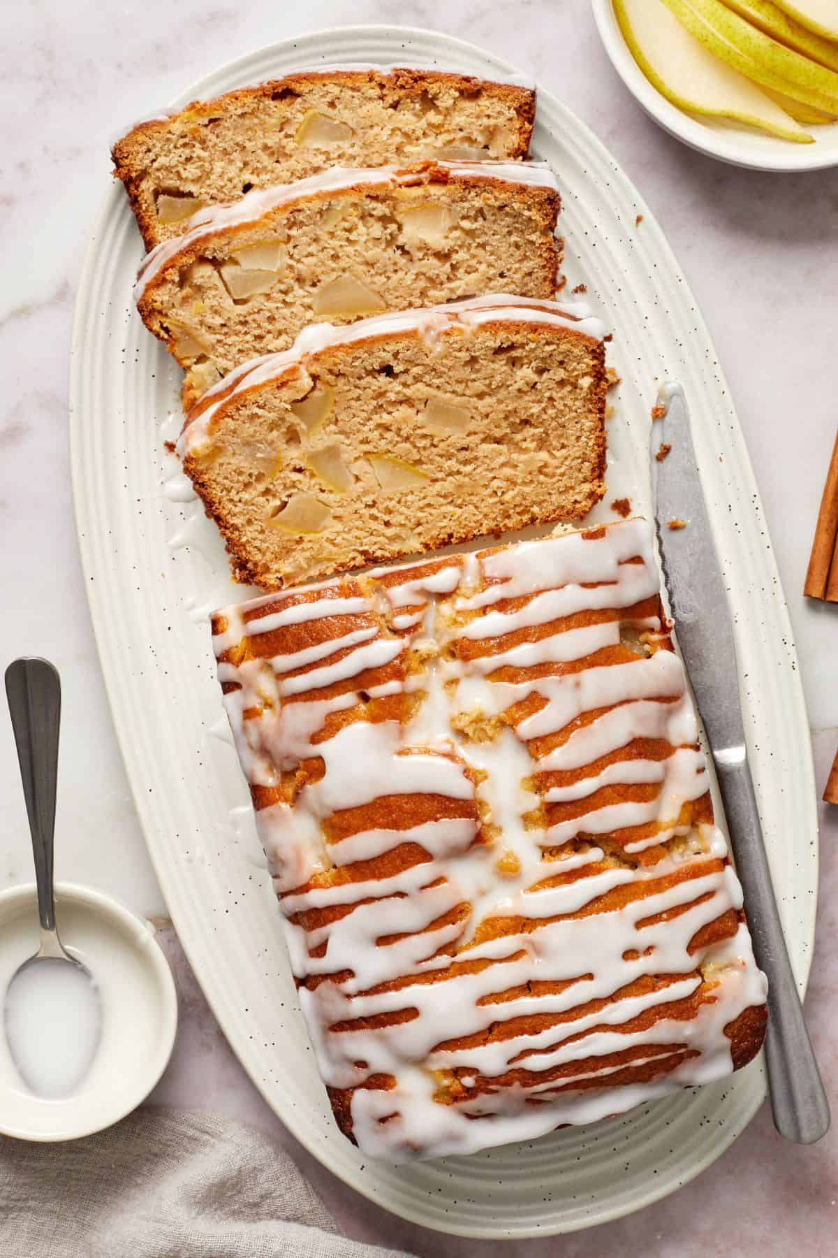 Pear Loaf Cake, with three slices cut, sitting on a white oval platter, with a knife on the side.