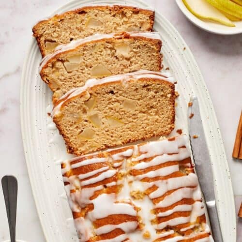 Pear Loaf Cake, with three slices cut, sitting on a white oval platter, with a knife on the side.