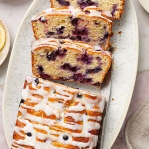 Blueberry Loaf Cake, with three slices cut, sitting on a white oval platter, with a knife on the side.