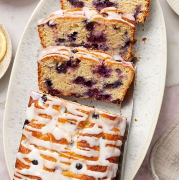 Blueberry Loaf Cake, with three slices cut, sitting on a white oval platter, with a knife on the side.