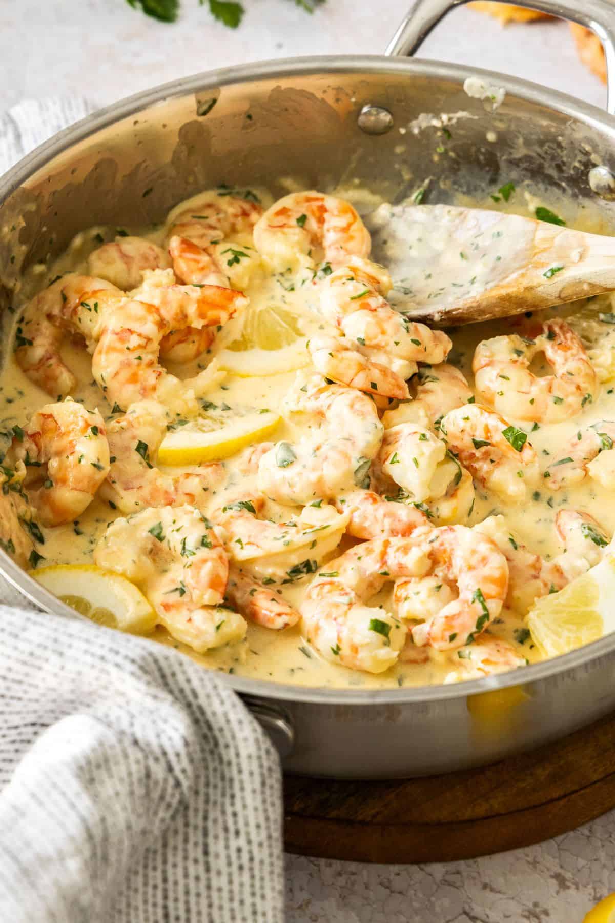 Frying pan with Creamy Lemon Prawns, and a wooden spoon resting in the pan.