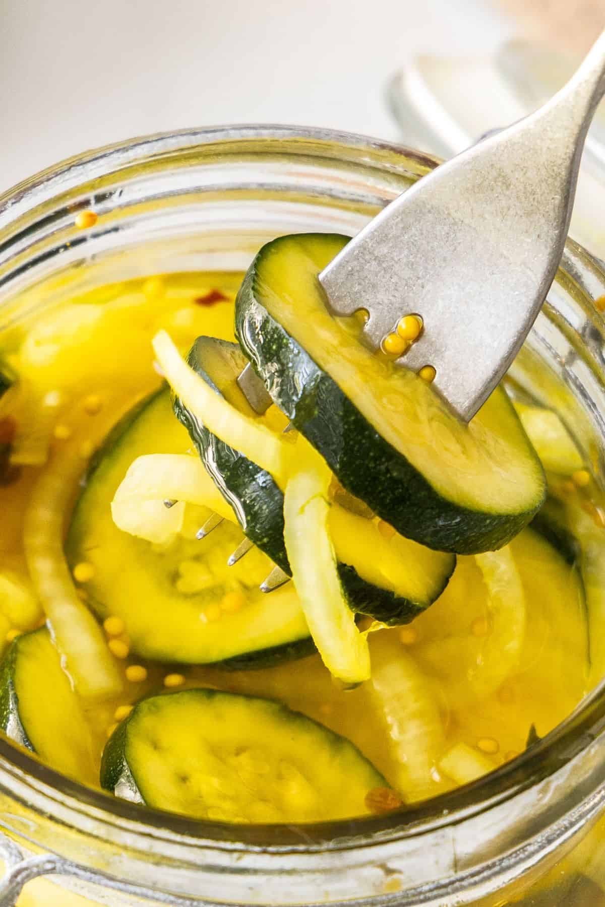 Fork reaching into jar of Pickled Zucchini to remove some pieces.