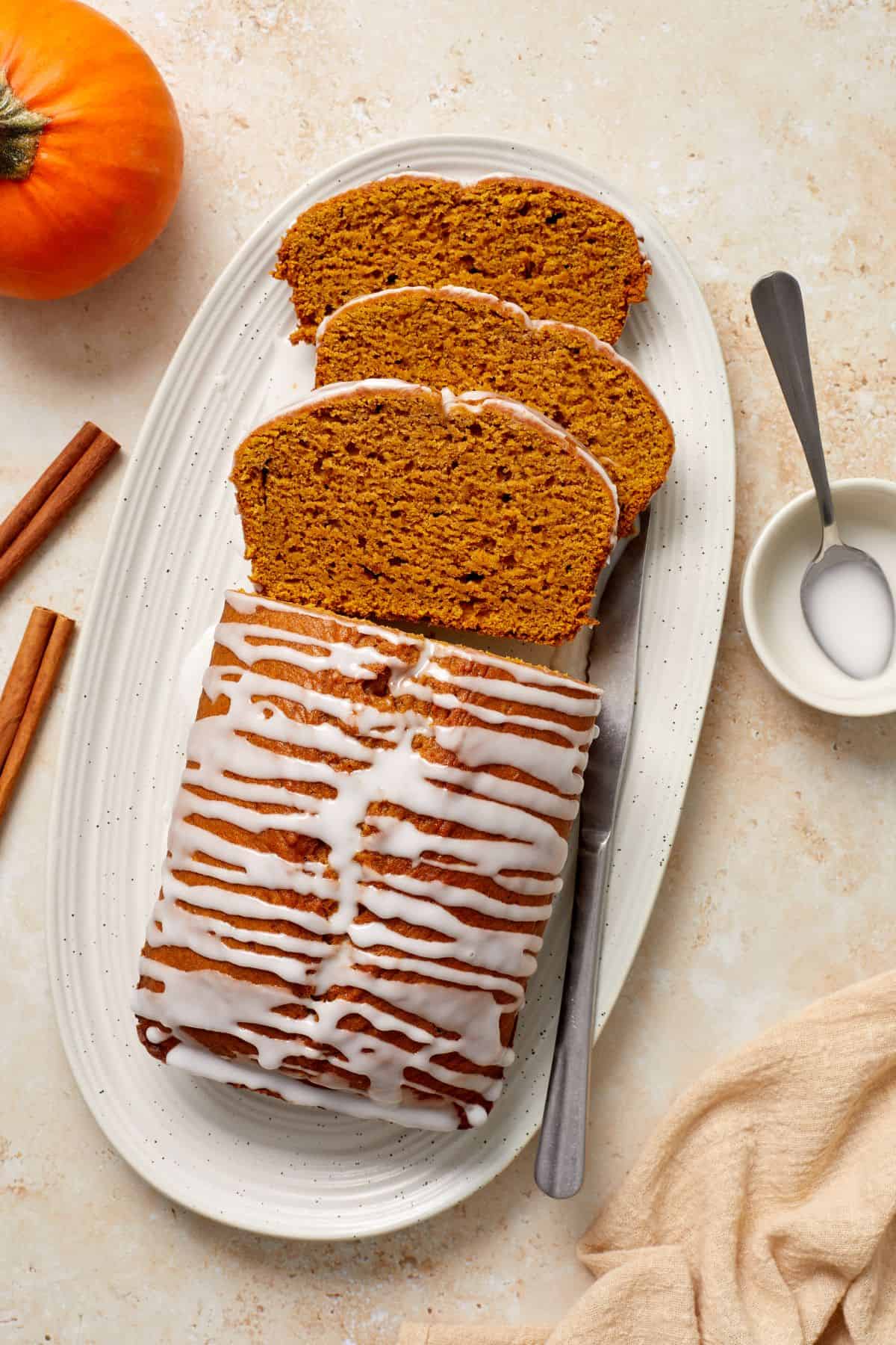 Pumpkin Loaf Cake, with three slices cut, sitting on a white oval platter, with a knife on the side.