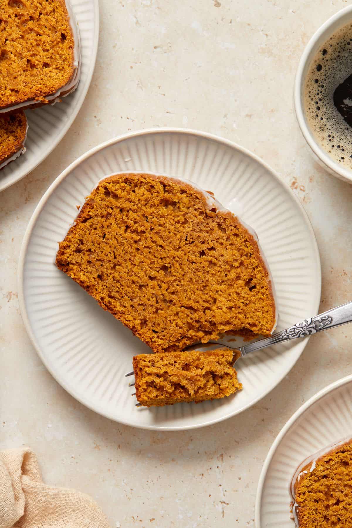 Slice of Pumpkin Loaf Cake on a small round white plate, with a fork cutting into it.