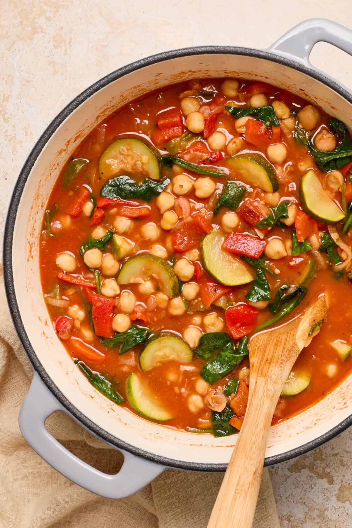 Large saucepan with Chickpea and Zucchini Stew, with a wooden spoon resting in it.