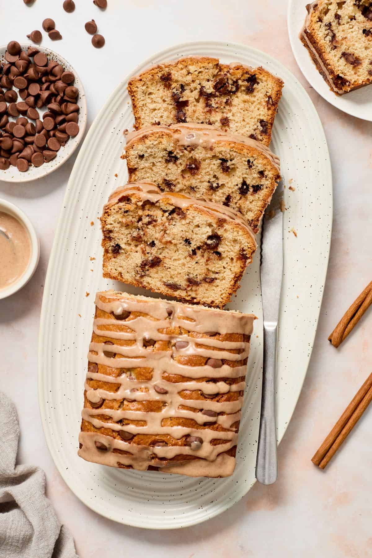 Cinnamon Chocolate Chip Loaf Cake, with four slices cut, sitting on a white oval platter, with a knife on the edge.