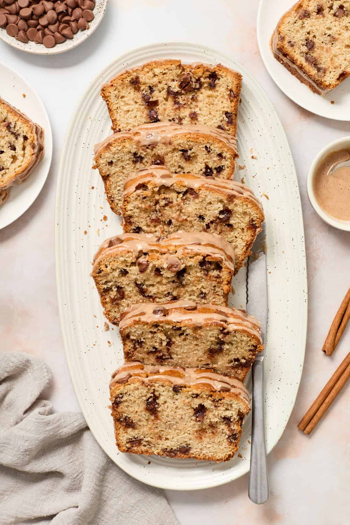 Slices of Cinnamon Chocolate Chip Loaf Cake arranged on a white oval platter, with a knife on the edge.