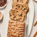 Cinnamon Chocolate Chip Loaf Cake, with four slices cut, sitting on a white oval platter, with a knife on the edge.