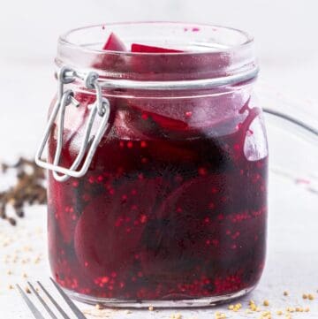 Glass jar of Pickled Beetroot, with a fork next to the jar, and some spices around the edge.