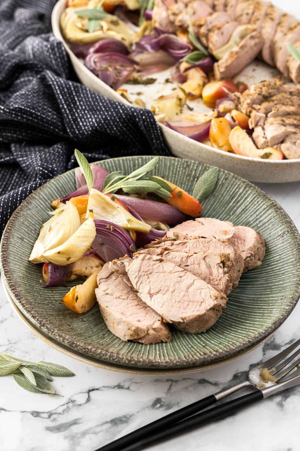 Serving of Roasted Pork Tenderloin, with the vegetables on the side, and the platter of meat in the background.