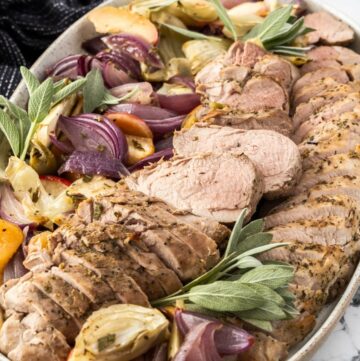 Platter of Roasted Pork Tenderloin, surrounded by pieces of apple, fennel, onion and sage.
