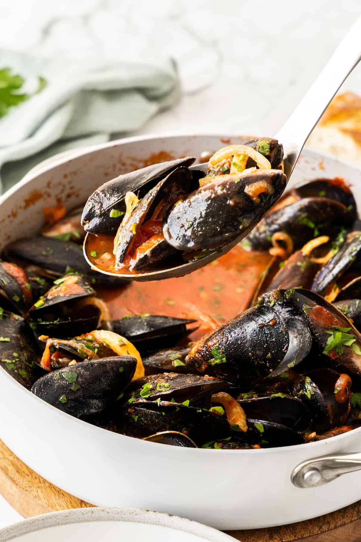 A spoon lifting up a serve of Mussels in Tomato Sauce.