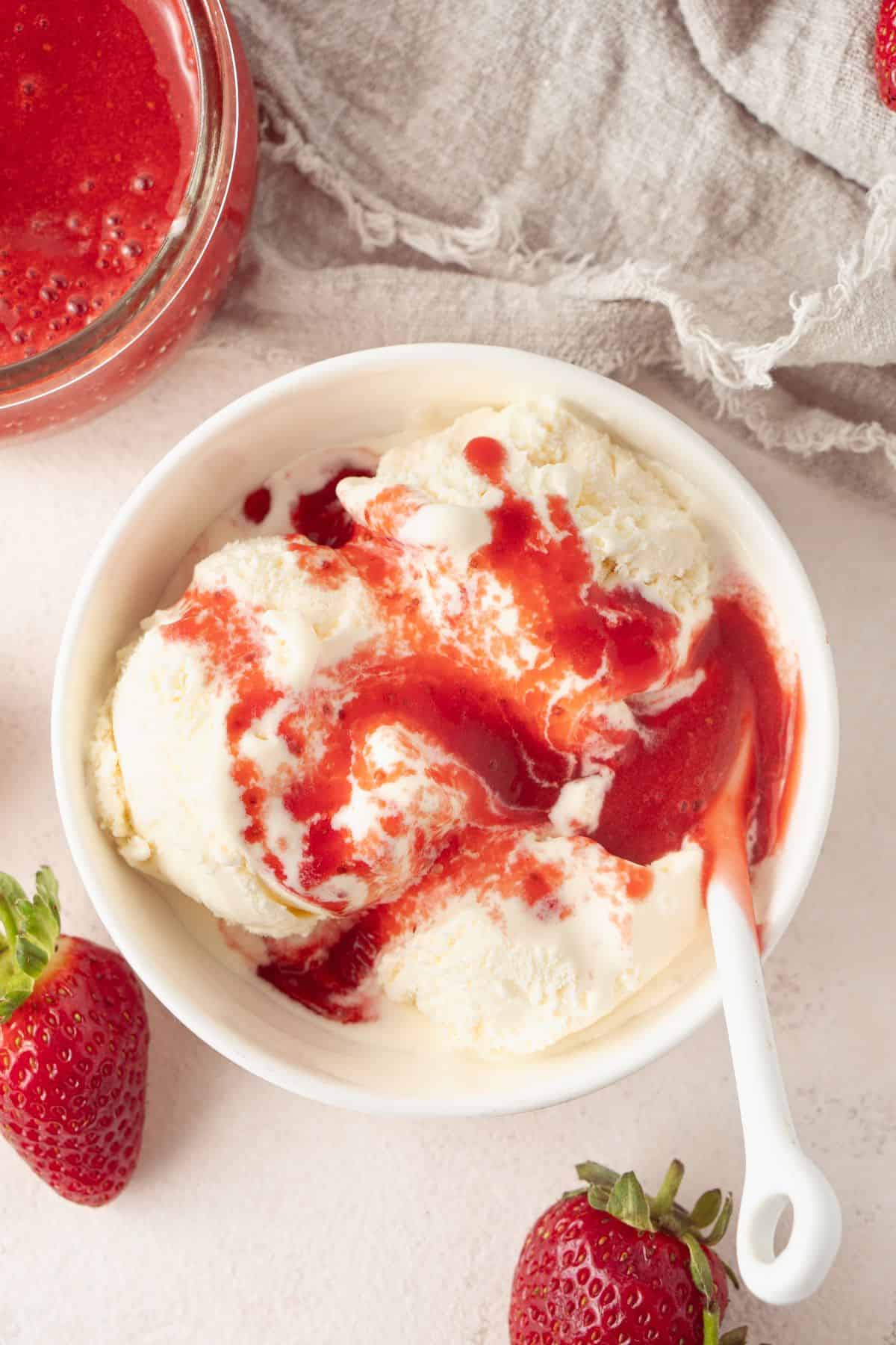 Dish of vanilla ice cream, topped with some strawberry sauce.