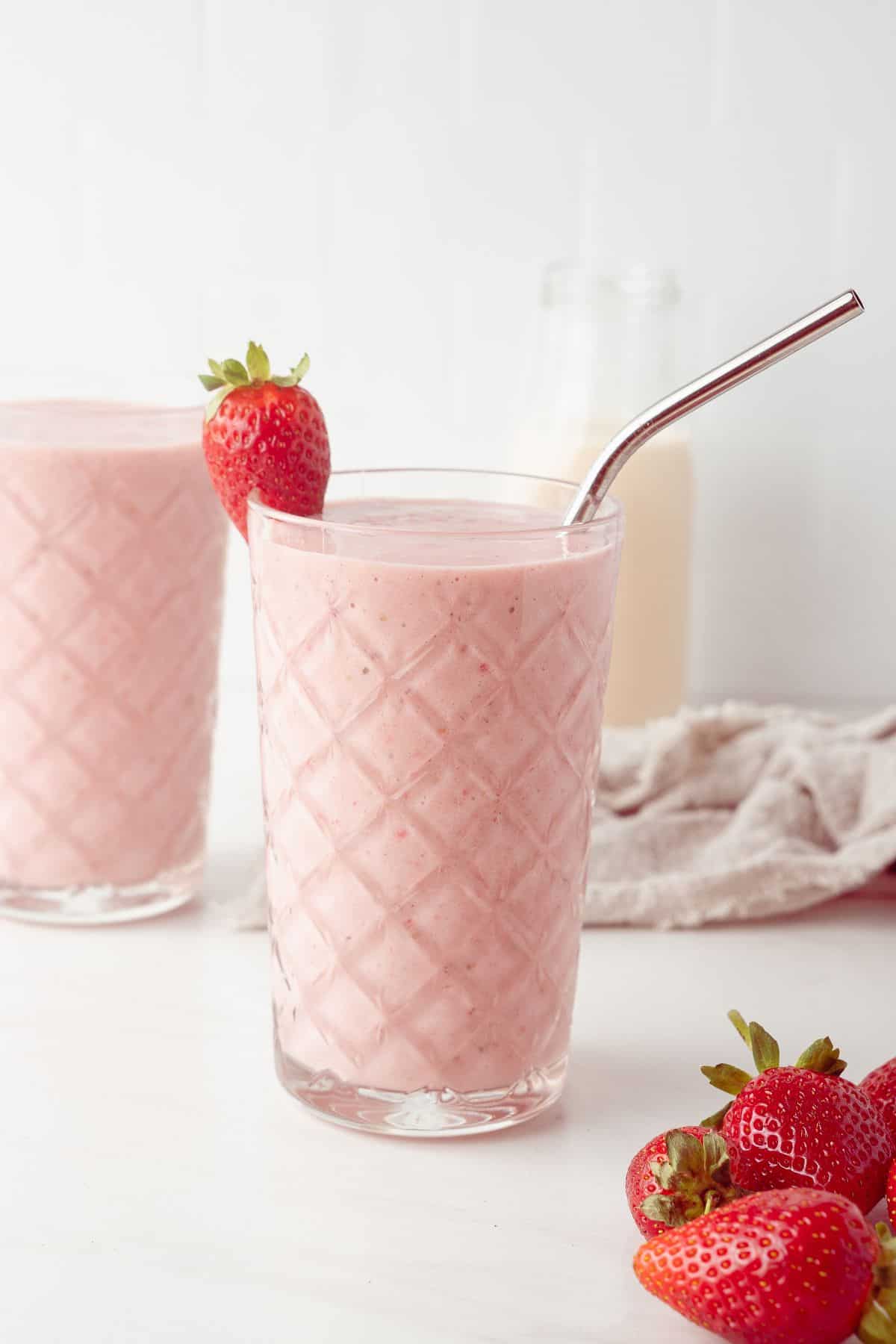 Two glasses full of Strawberry and Banana Smoothie, one with a straw, with some strawberries around the edge.