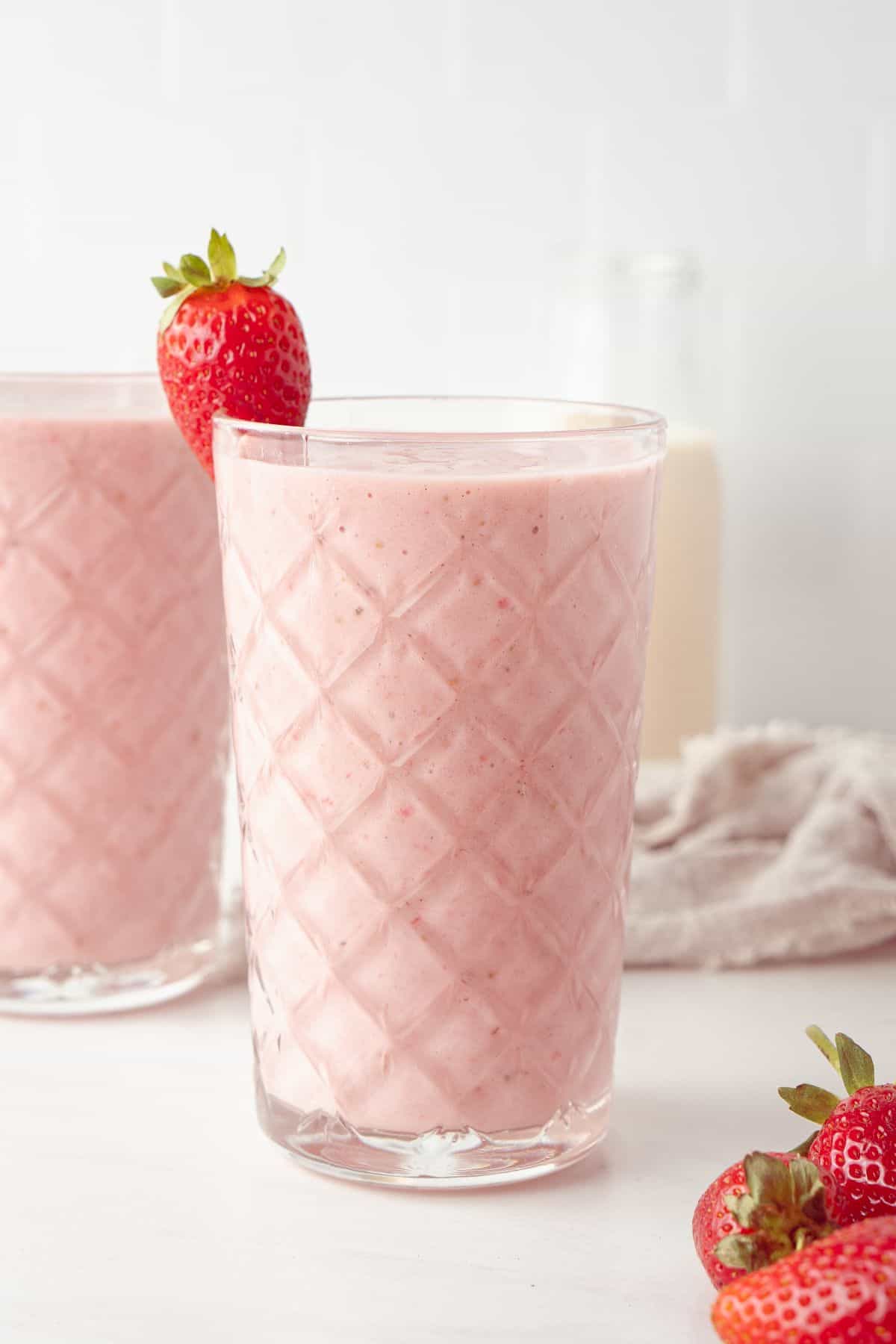 Two glasses full of Strawberry and Banana Smoothie, with a strawberry on the edge of the glass.