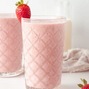 Two glasses full of Strawberry and Banana Smoothie, with a strawberry on the edge of the glass.