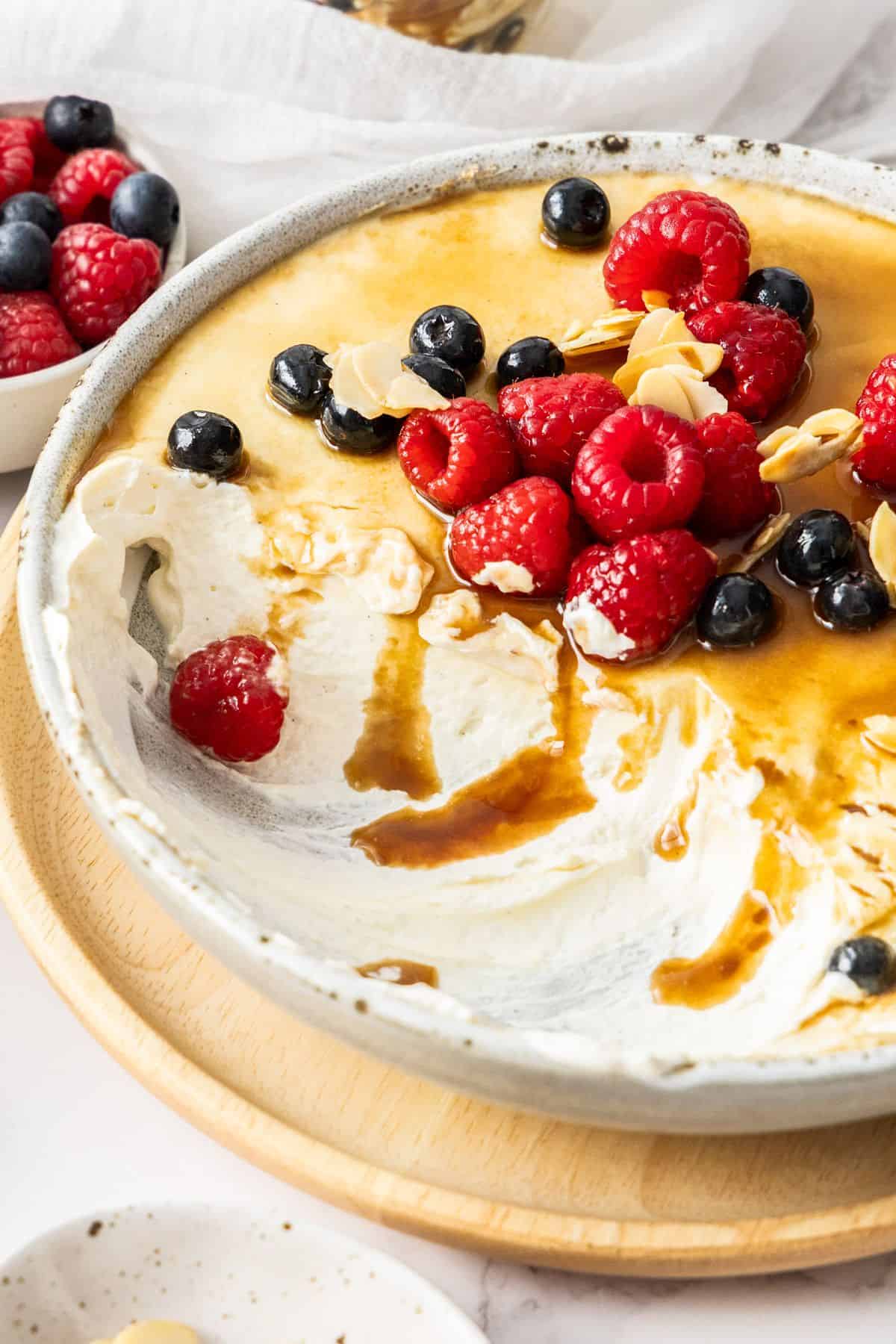 Round dish containing Caramelised Yoghurt Cream, garnished with mixed berries and flaked almonds, with a serve scooped out.
