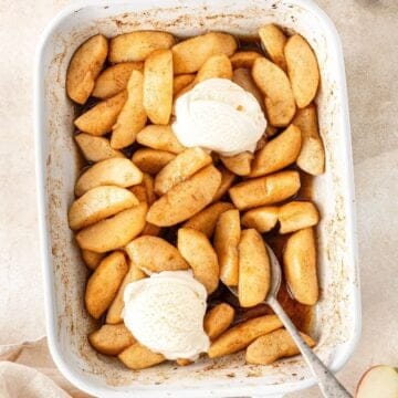 Rectangular white baking dish with the cooked Baked Apples, two scoops of ice cream and a spoon resting in the dish.