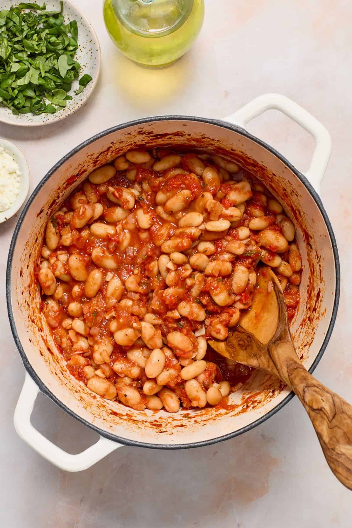 Saucepan with Mediterranean Baked Beans, with a wooden spoon resting in the pot.