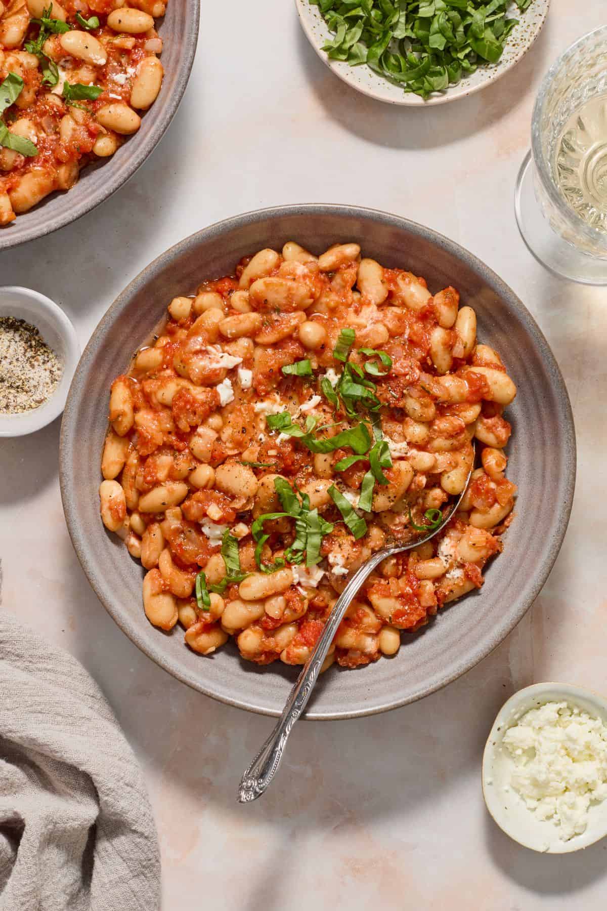 Round grey bowl with a serve of Mediterranean Baked Beans, garnished with torn fresh basil.