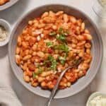 Round grey bowl with a serve of Mediterranean Baked Beans, garnished with torn fresh basil.