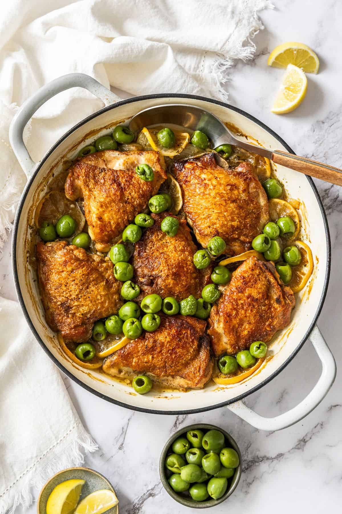 Round dish with the Braised Chicken,, Lemon and Olives, with a spoon resting in the dish.