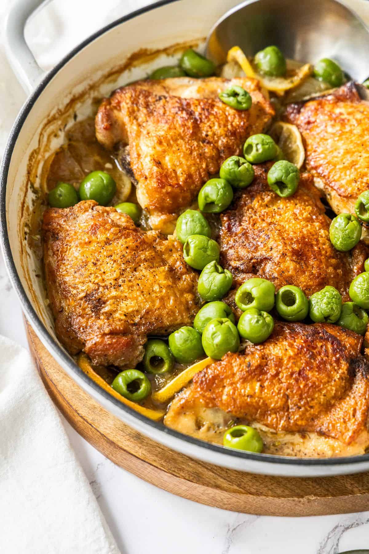 Round dish with the Braised Chicken,, Lemon and Olives, with a spoon resting in the dish.