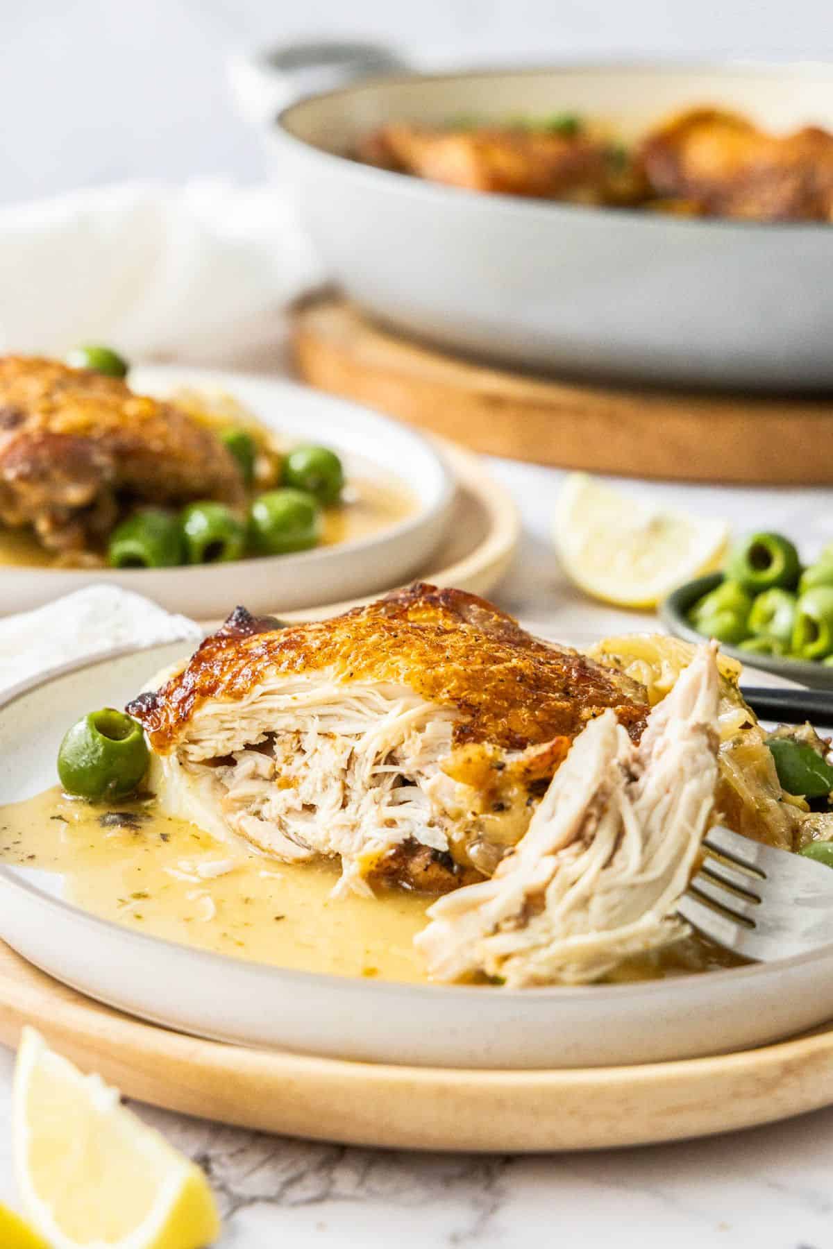 A serve of Braised Chicken on a white plate, with the thigh cut into to show the inside of the chicken.