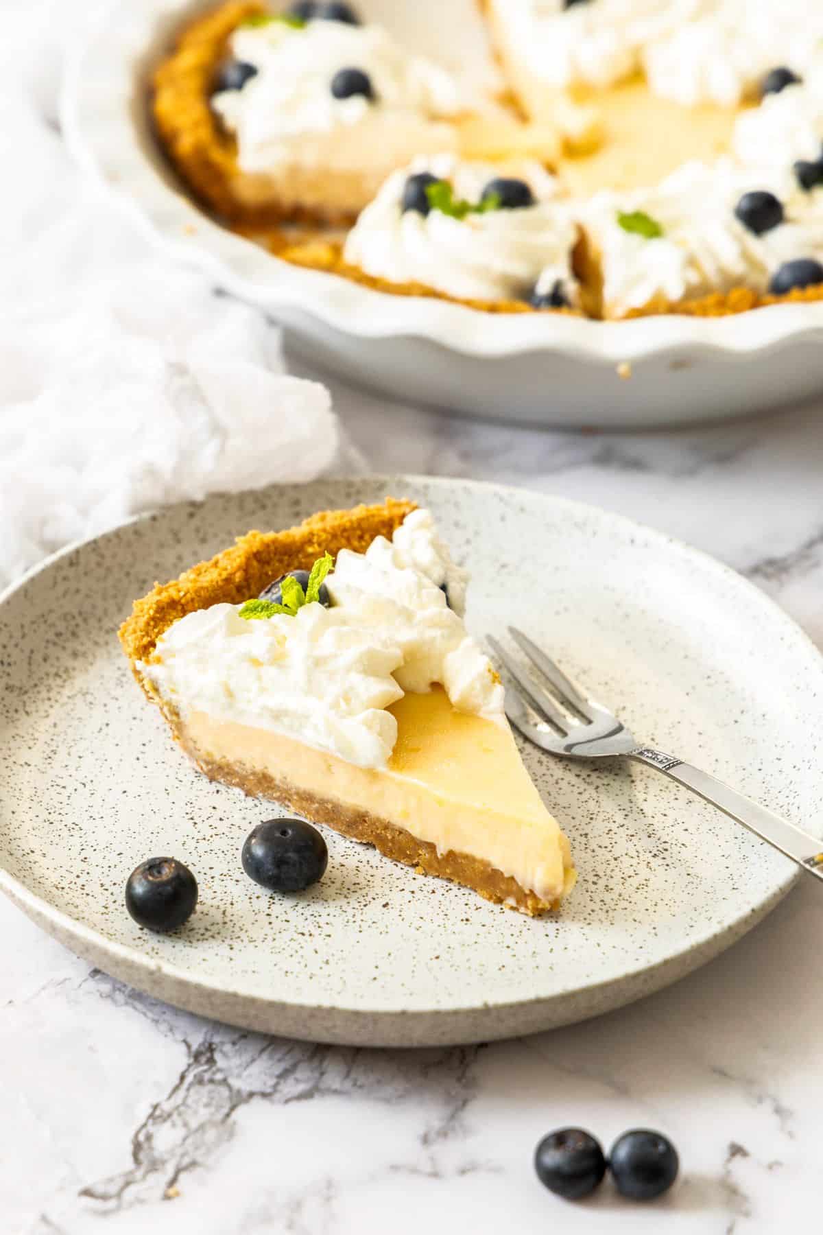 Slice of Creamy Lemon Pie on a round white speckled plate, with a fork on the side.