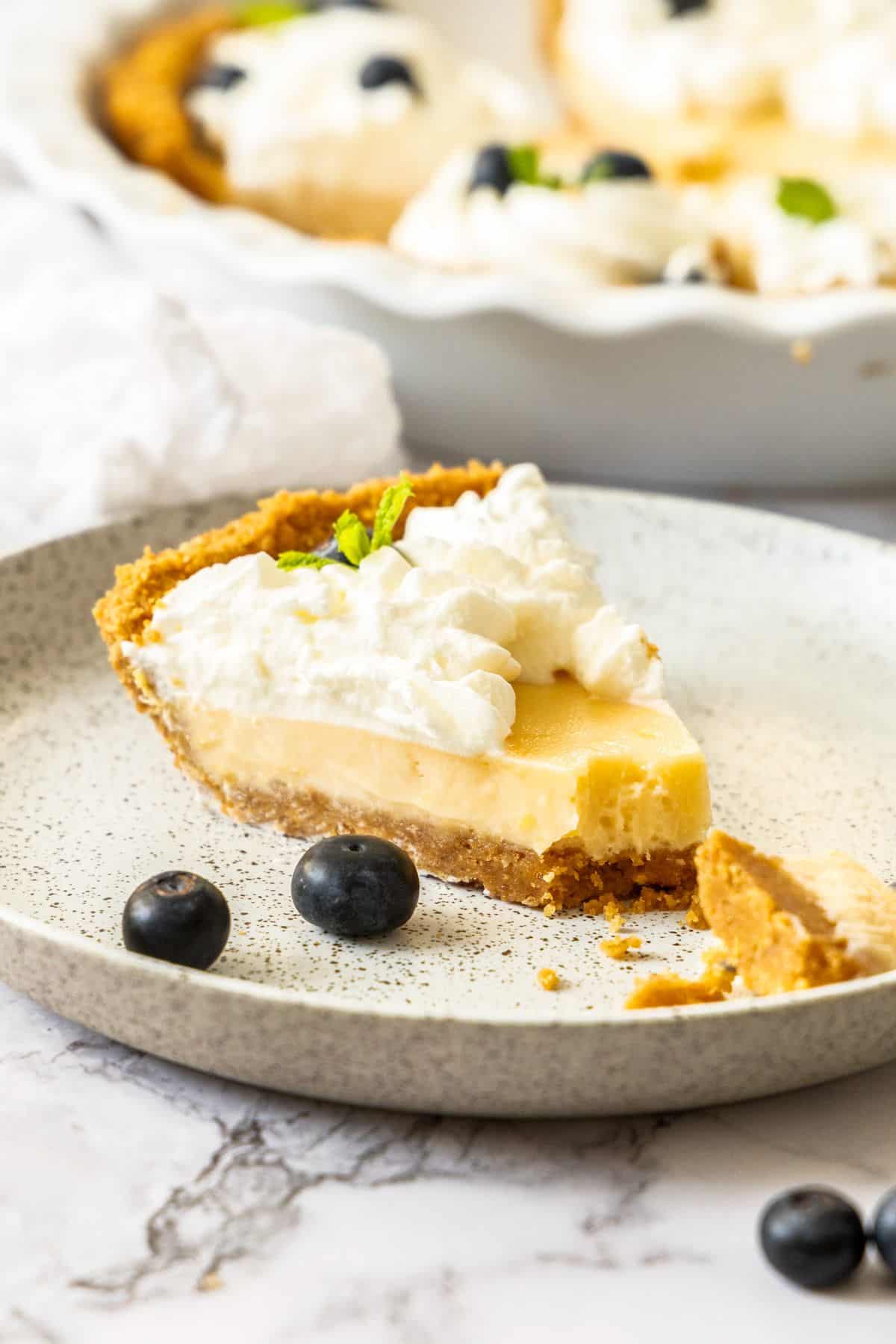 Slice of Creamy Lemon Pie on a round white speckled plate, with a piece cut out of it to show the texture.