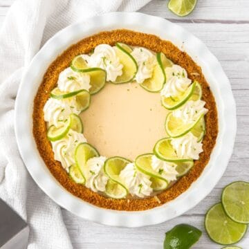 Whole Creamy Lime Pie, garnished with lime slices and whipped cream, sitting on a white cloth.