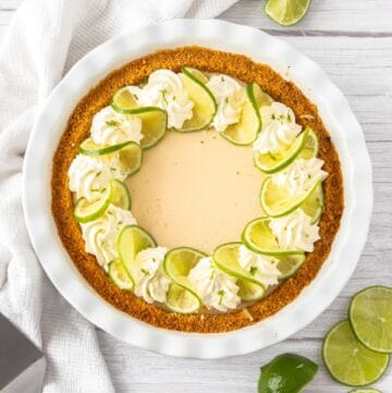 Whole Creamy Lime Pie, garnished with lime slices and whipped cream, sitting on a white cloth.